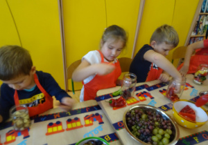 trójka dzieci wkłada w słoiki różne warzywa m.in. paprykę oraz owoce